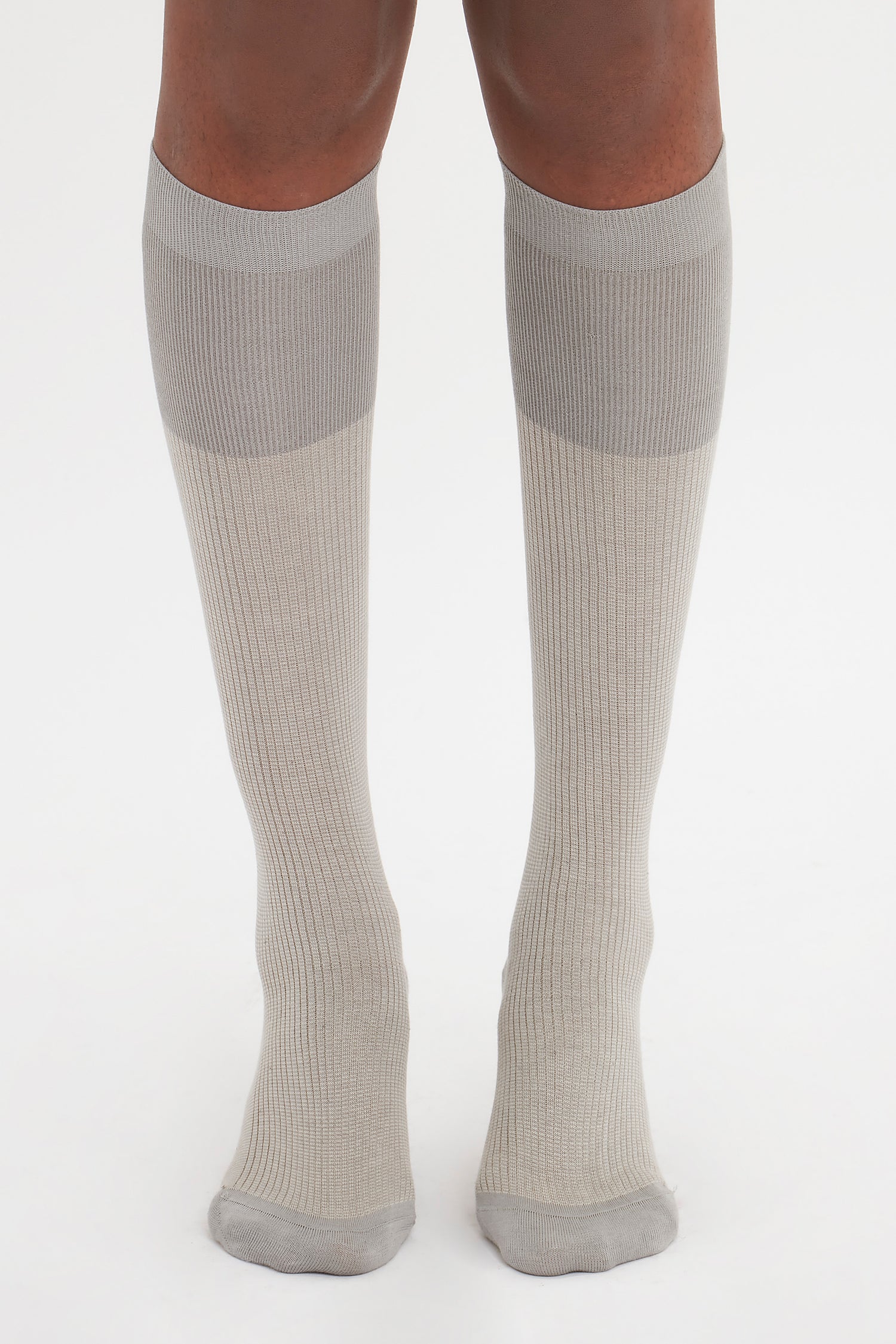 The image shows a pair of legs wearing knee-high, light gray Superfine Rib Socks In Lunar Grey by Victoria Beckham made from 100% cotton, standing on a white background—an elevated wardrobe essential for any day.