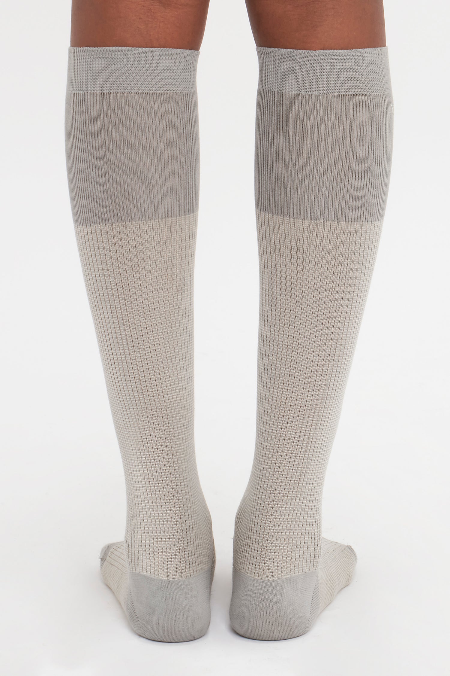 Back view of a person wearing knee-high, light gray Superfine Rib Socks In Lunar Grey by Victoria Beckham standing on a white background—an elevated wardrobe essential in 100% cotton.