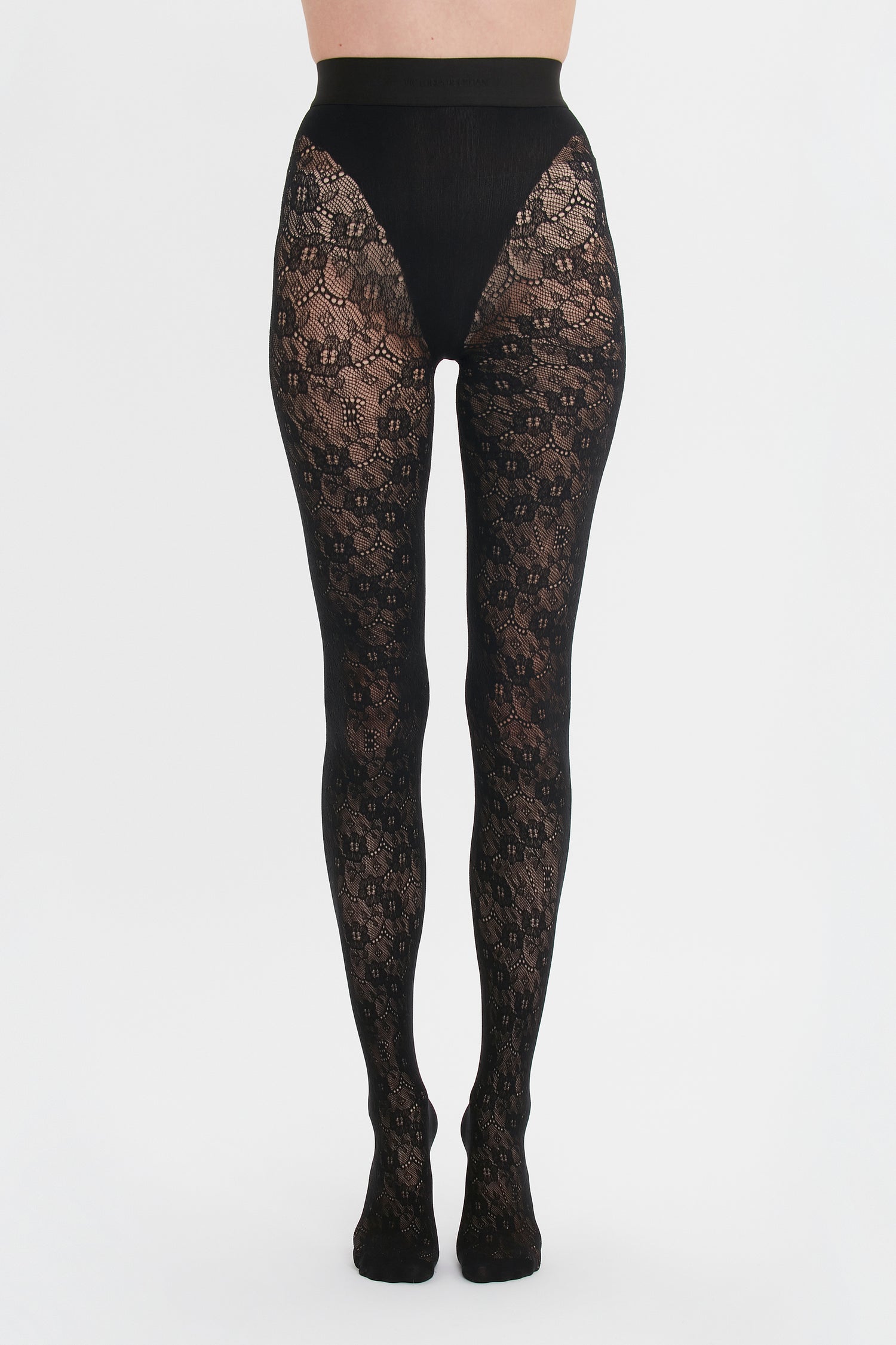 A person wearing decorative Victoria Beckham Exclusive VB Monogram Lace Tights In Black against a white background.