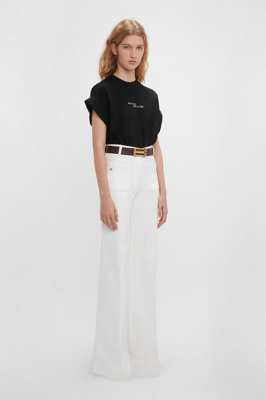 A woman in a Victoria Beckham 'Do As I Say, Not As I Do' Slogan T-shirt in black and white high-waisted trousers stands against a plain background.