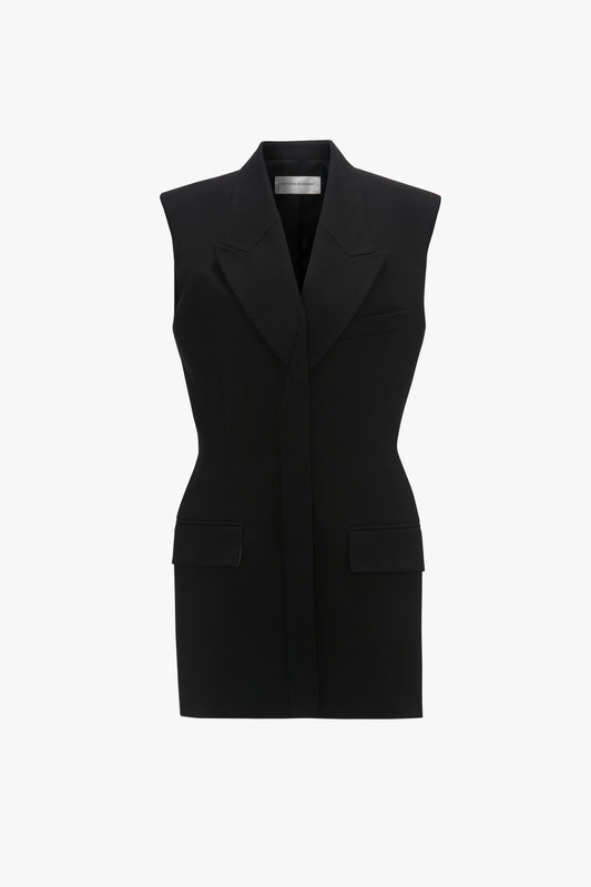 A sleeveless black tuxedo vest with a v-neckline, front buttons, and flap pockets, crafted from a recycled wool blend, displayed against a white background by Victoria Beckham.