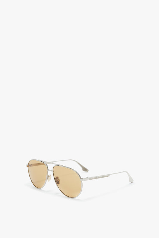 A pair of Victoria Beckham V Metal Pilot Sunglasses In Silver-Brown with gold-tinted lenses and a thin silver frame, featuring adjustable nose pads, isolated on a white background.