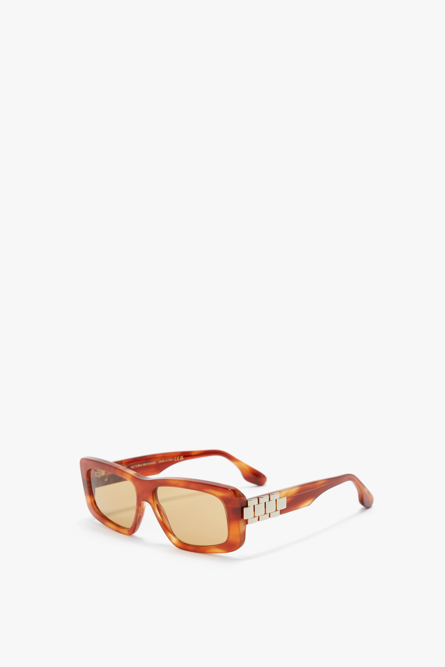 Rectangular amber-colored sunglasses with tinted lenses and metal decorative accents on the temples, embodying the sophisticated style of Victoria Beckham eyewear. The Chain Detail Rectangular Frame Sunglasses In Striped Blonde Havana is elegantly showcased against a pristine white background.