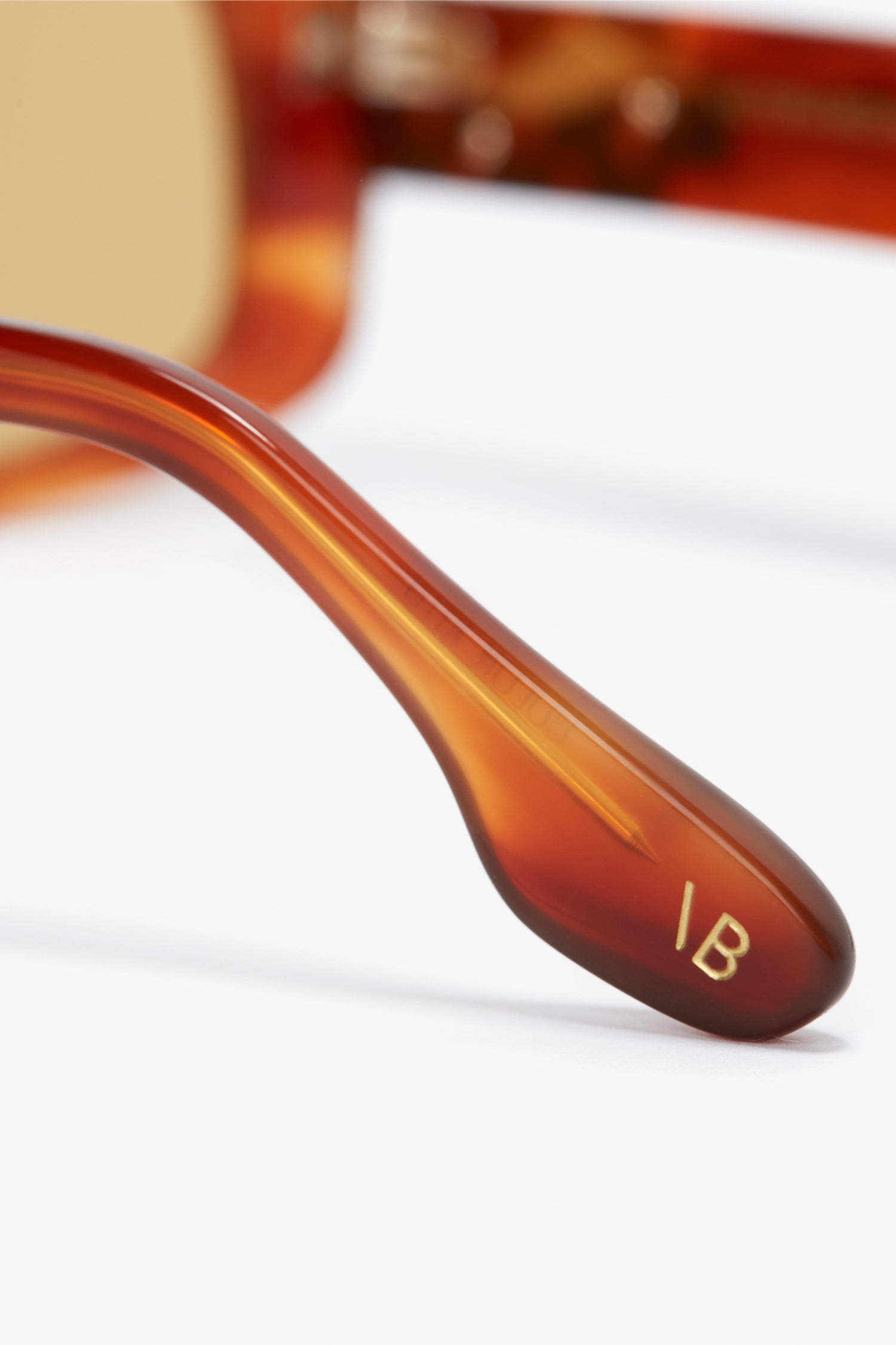 Close-up of the arm of a pair of Victoria Beckham Chain Detail Rectangular Frame Sunglasses In Striped Blonde Havana, with the initials "IB" engraved in gold on the end of the arm.