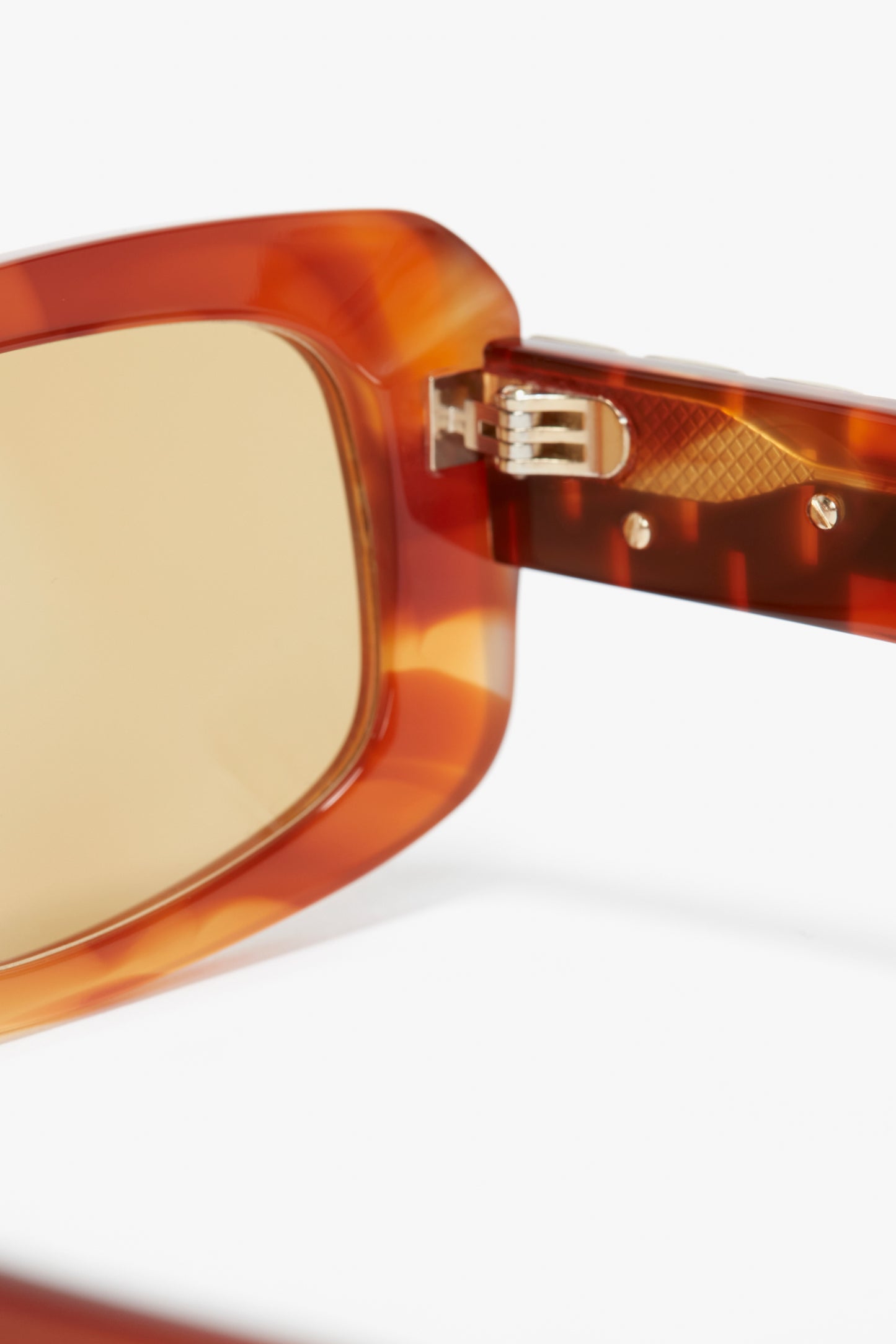 Close-up of the hinge detail on a pair of Victoria Beckham Chain Detail Rectangular Frame Sunglasses In Striped Blonde Havana.