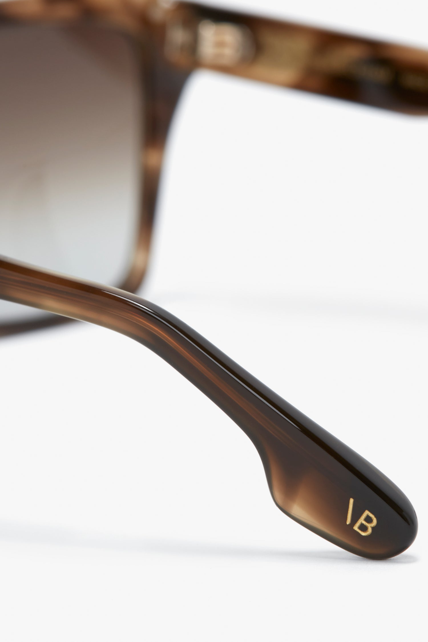 Close-up of Victoria Beckham eyewear reveals the intricate arm detail of Soft Square Frame Sunglasses In Striped Khaki Havana, with "IB" elegantly engraved on the inside amid the Striped Khaki pattern.
