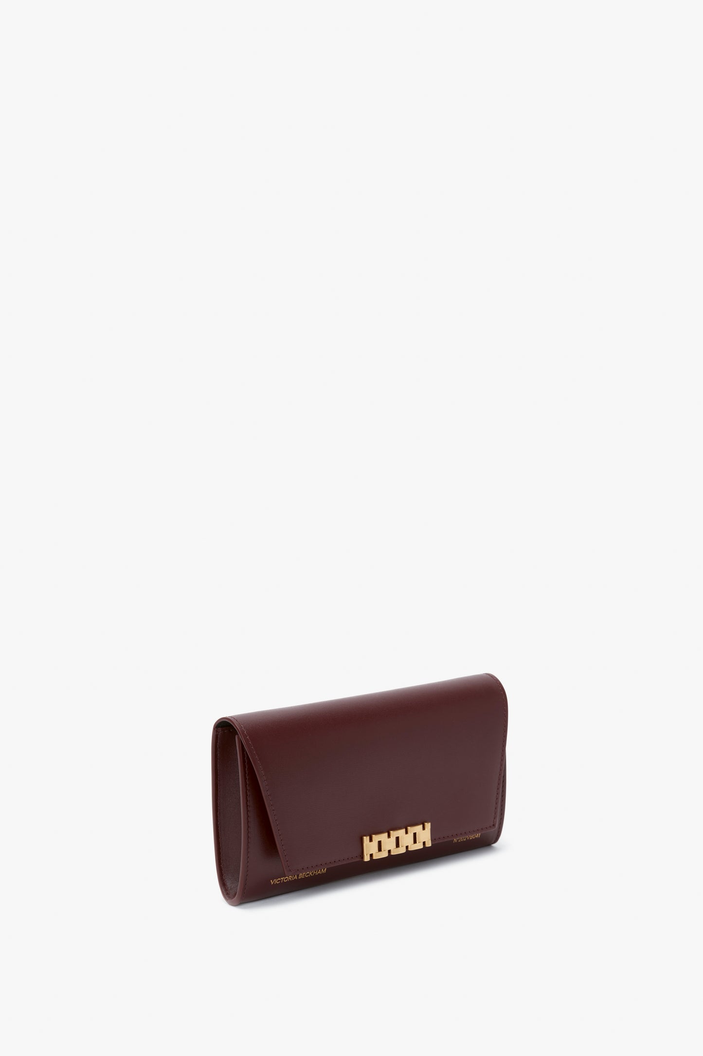A rectangular, dark brown leather Wallet On Chain In Burgundy Leather by Victoria Beckham with a gold geometric clasp and discreet branding, complemented by a detachable gold chain, placed against a plain white background.