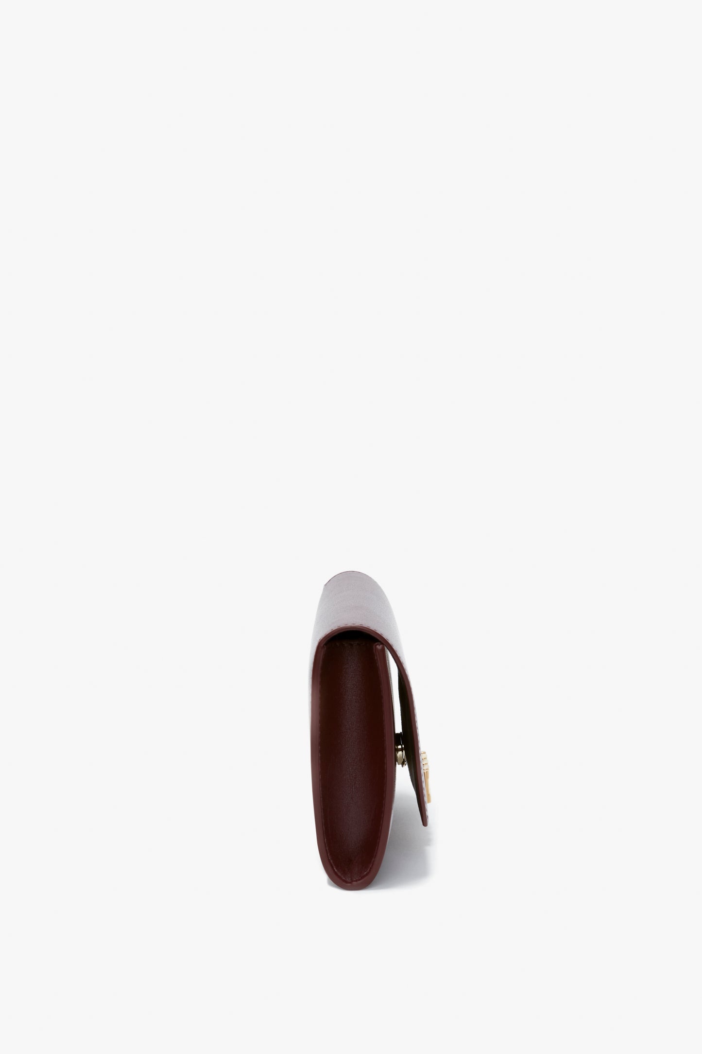 Side view of a closed Wallet On Chain In Burgundy Leather by Victoria Beckham with a golden clasp and an elegant gold chain, shown against a white background.