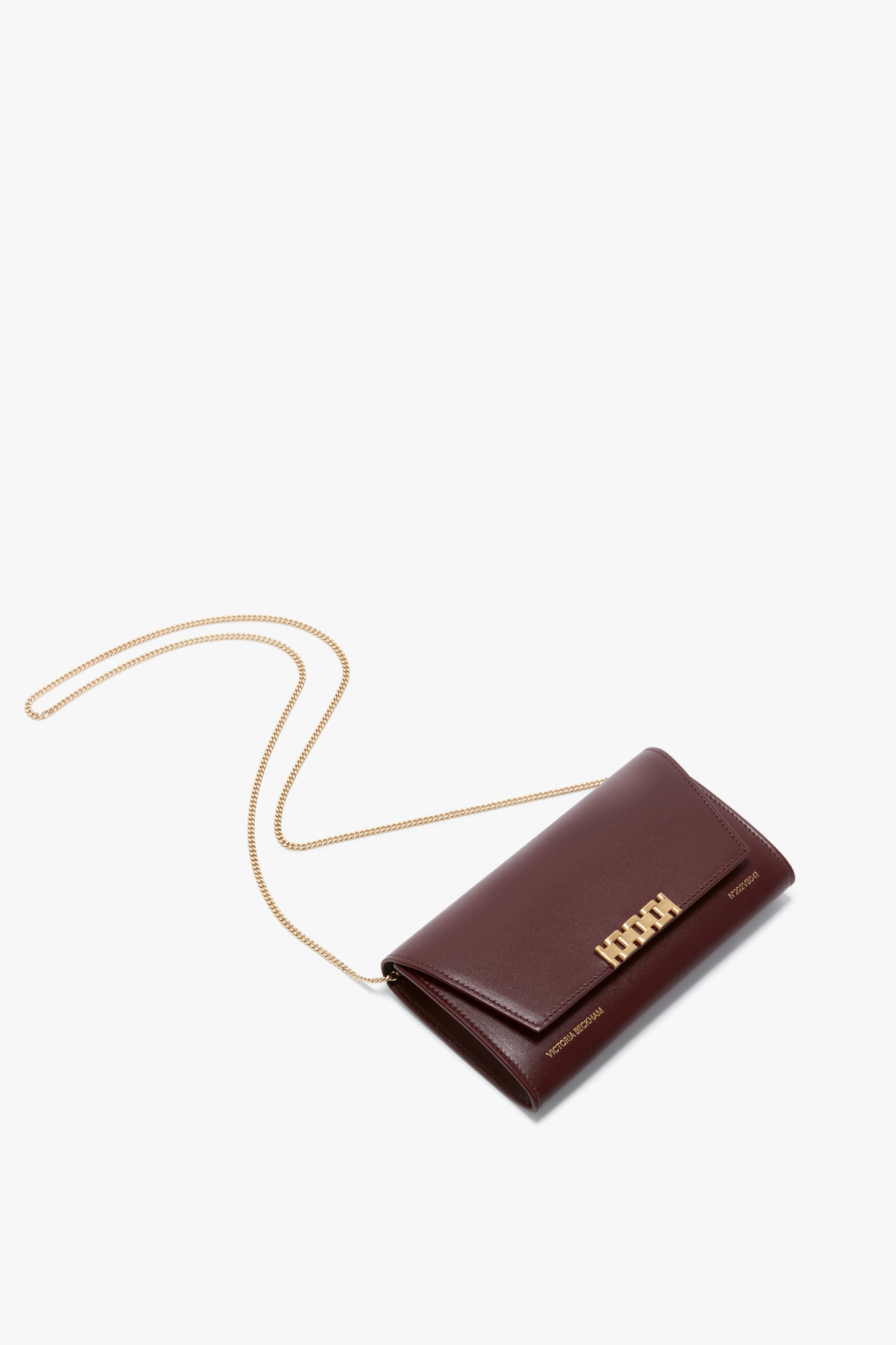 A Wallet On Chain In Burgundy Leather by Victoria Beckham with a gold chain strap and gold clasp is displayed against a white background.