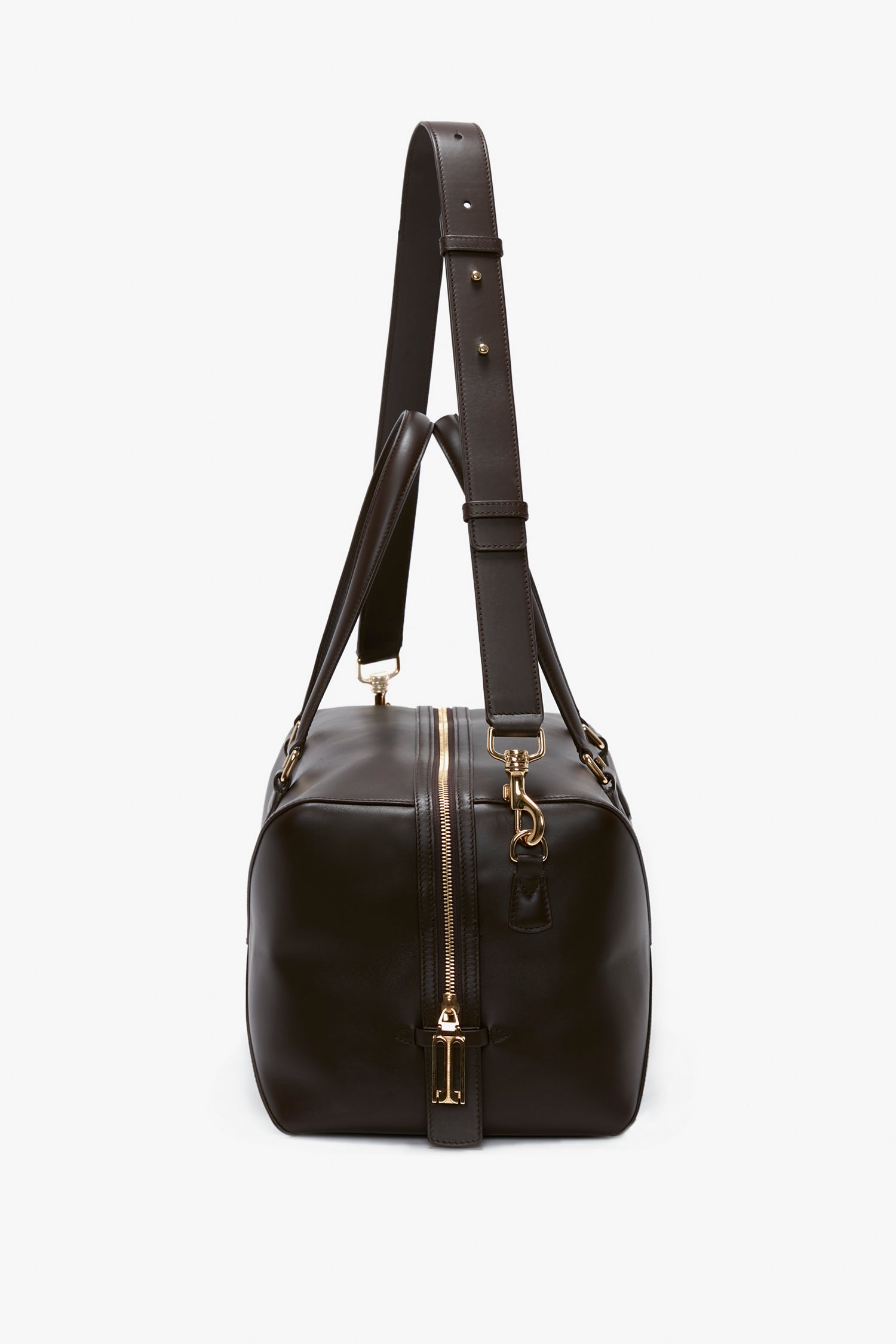 A Medium Gym Bag In Chocolate Brown with a shoulder strap and gold hardware, standing upright against a white background, reminiscent of Victoria Beckham's timeless style.