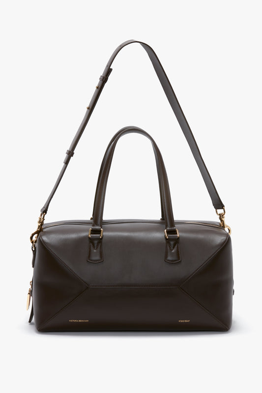 A Medium Gym Bag In Chocolate Brown by Victoria Beckham with gold hardware, featuring two top handles and an adjustable shoulder strap, inspired by the stylish designs of Victoria Beckham.