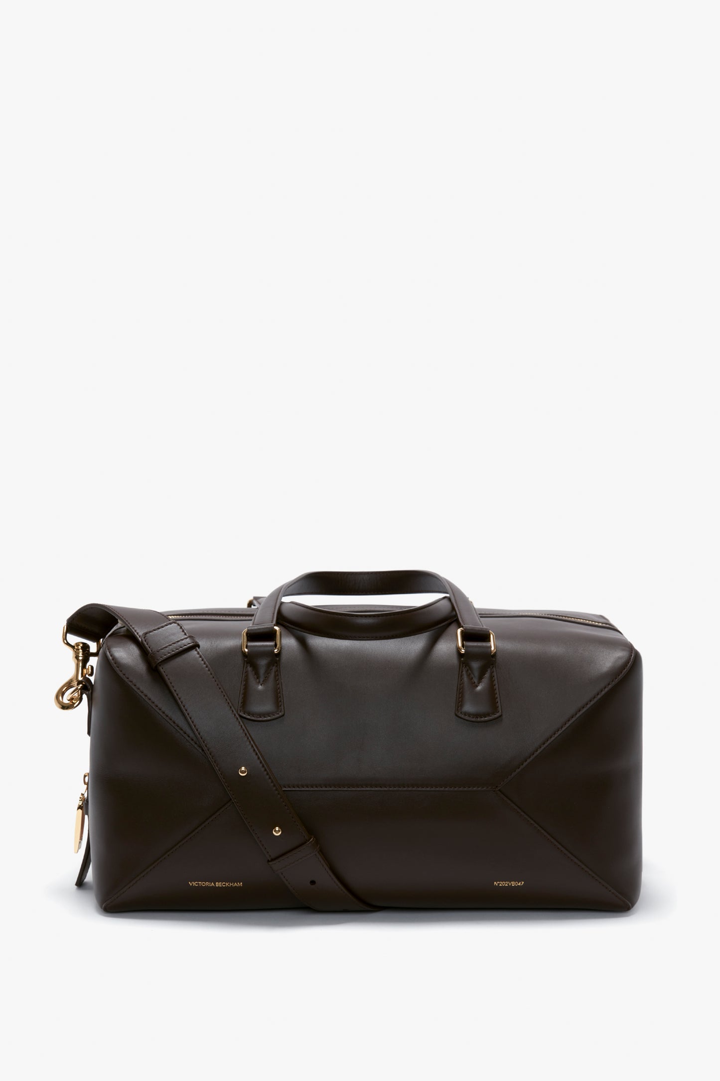 A sleek, Medium Gym Bag In Chocolate Brown by Victoria Beckham made from calfskin with gold hardware, short handles, and a detachable shoulder strap, displayed against a white background.