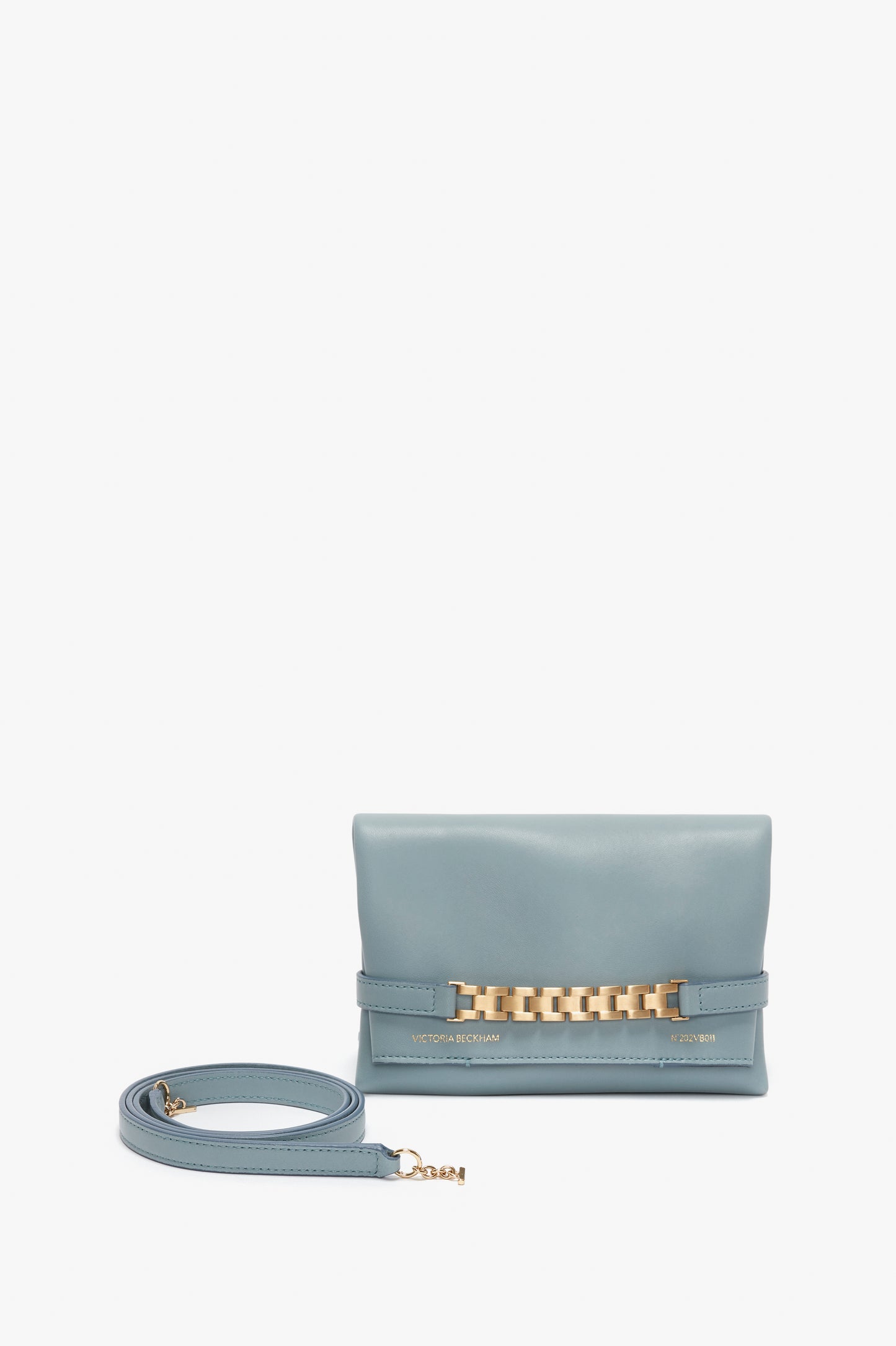 A Mini Chain Pouch Bag With Long Strap In Ice Leather with a gold-tone chain accent and "Victoria Beckham" branding. The image also shows a detachable strap with a gold clasp placed beside the bag, enhancing its versatility.