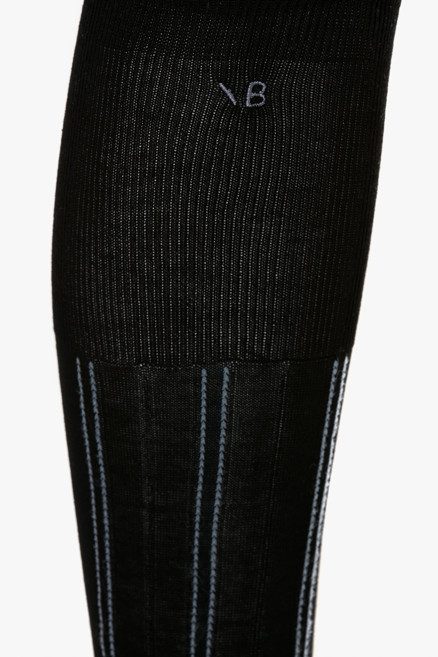 Close-up of a black ribbed sock with gray vertical stripes and the letters "V B" stitched on the upper part, showcasing its contemporary design. The Victoria Beckham Superfine Rib Socks In Black like these are a wardrobe essential for any modern closet.