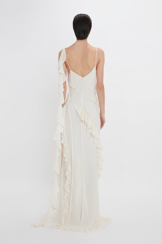 A woman viewed from behind wearing an elegant white Victoria Beckham Exclusive Asymmetric Bias Frill Dress In Ivory with spaghetti straps, against a plain white background.