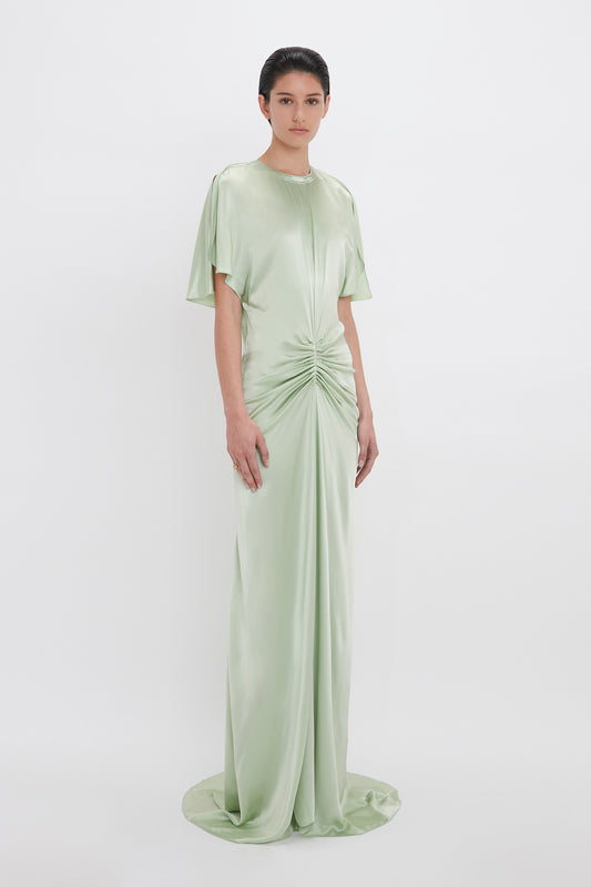A woman models an Exclusive Floor-Length Gathered Dress in Jade by Victoria Beckham, with short sleeves and a ruched front, standing against a plain white background.