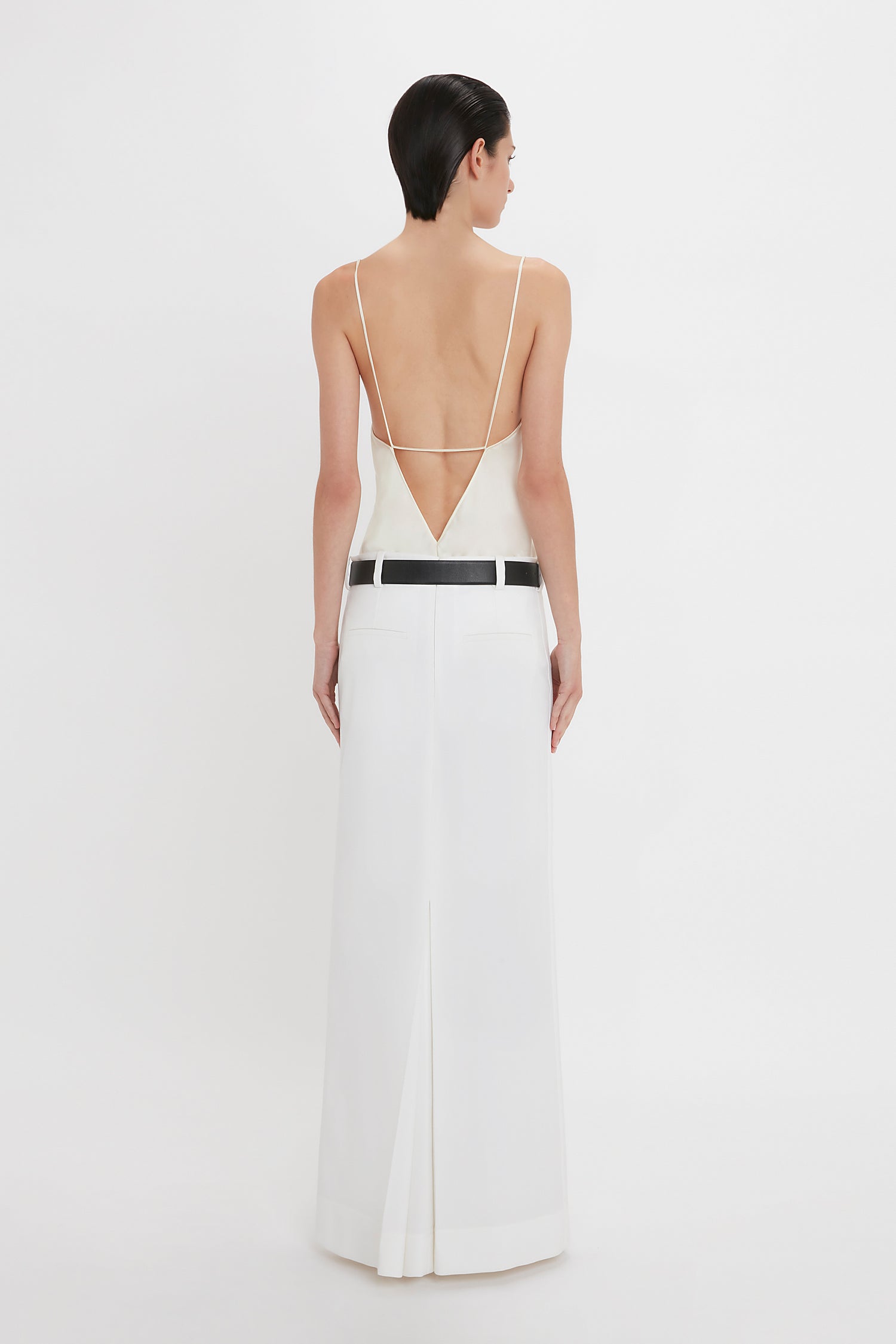 A person with short dark hair is wearing an Exclusive Cami Top In Ivory by Victoria Beckham that is made of silk and extends to the floor. The top features a black belt around the waist. They are facing away from the camera.