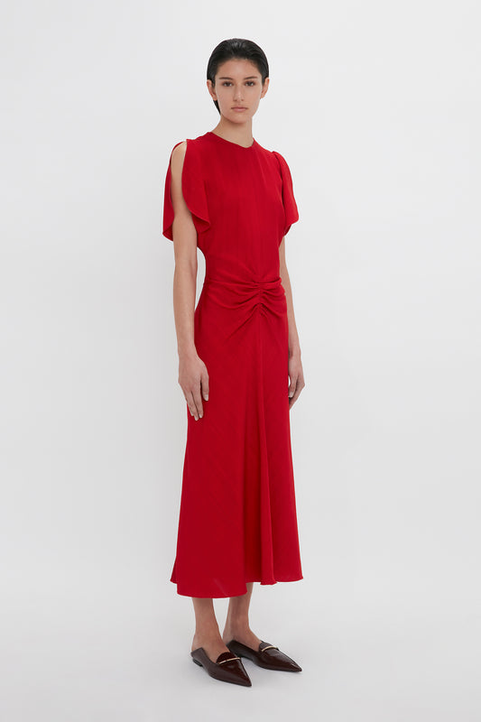 Woman in a Victoria Beckham Exclusive Gathered V-Neck Midi Dress In Carmine, standing against a white background.