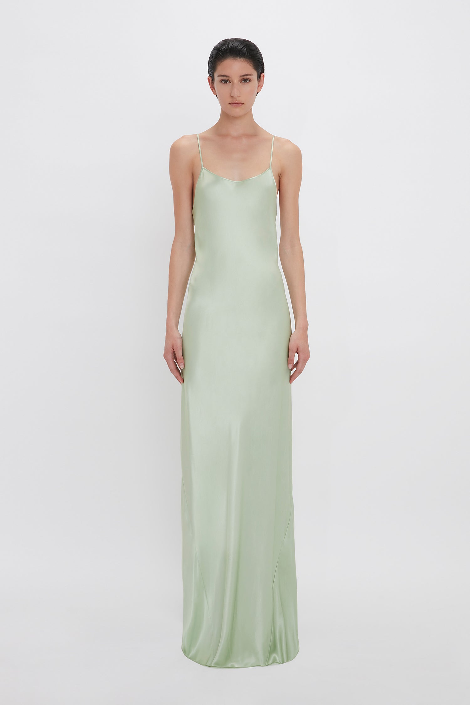 A woman in a Victoria Beckham Exclusive Low Back Cami Floor-Length Dress In Jade stands against a white background, looking directly at the camera.
