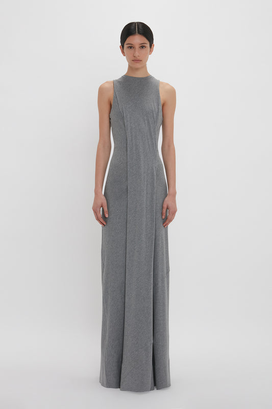 A woman in a long, sleeveless Victoria Beckham Frame Detailed Maxi Dress In Titanium stands against a white backdrop, looking directly at the camera.