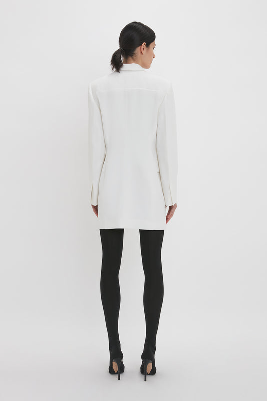 A woman from behind wearing a Victoria Beckham Exclusive Fold Shoulder Detail Dress In Ivory and black tights, standing against a plain white background.