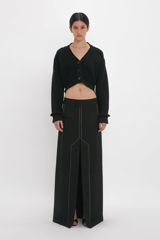 A woman in a Victoria Beckham cropped v-neck cardigan and high-waisted black trousers stands against a white background.
