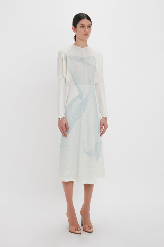 A woman in an elegant Victoria Beckham Long Sleeve Dolman Midi Dress In White-Blue Contorted Net stands against a plain white background.