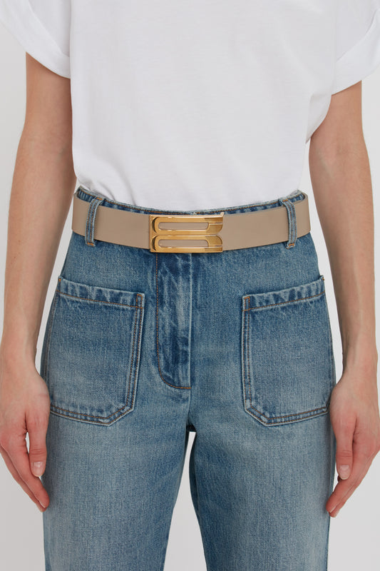 Close-up of a person wearing blue jeans with a Victoria Beckham Exclusive Jumbo Frame Belt in beige leather, focusing on the waist area and belt buckle.