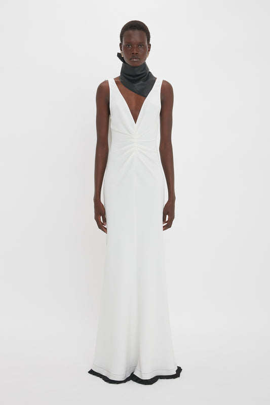 A person wearing a sleeveless white gown with a deep V-neckline and a black scarf stands against a plain white background, flawlessly emulating the sophisticated allure of an Exclusive V-Neck Gathered Waist Floor-Length Gown In Ivory from the Victoria Beckham brand.