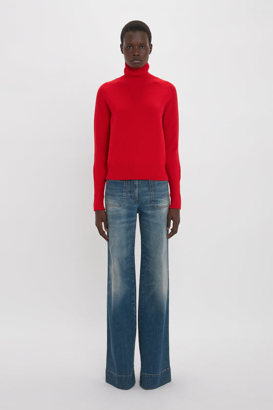 A black man wearing a red turtleneck sweater and Victoria Beckham's Alina Jean In Heavy Vintage Indigo Wash stands against a white background.