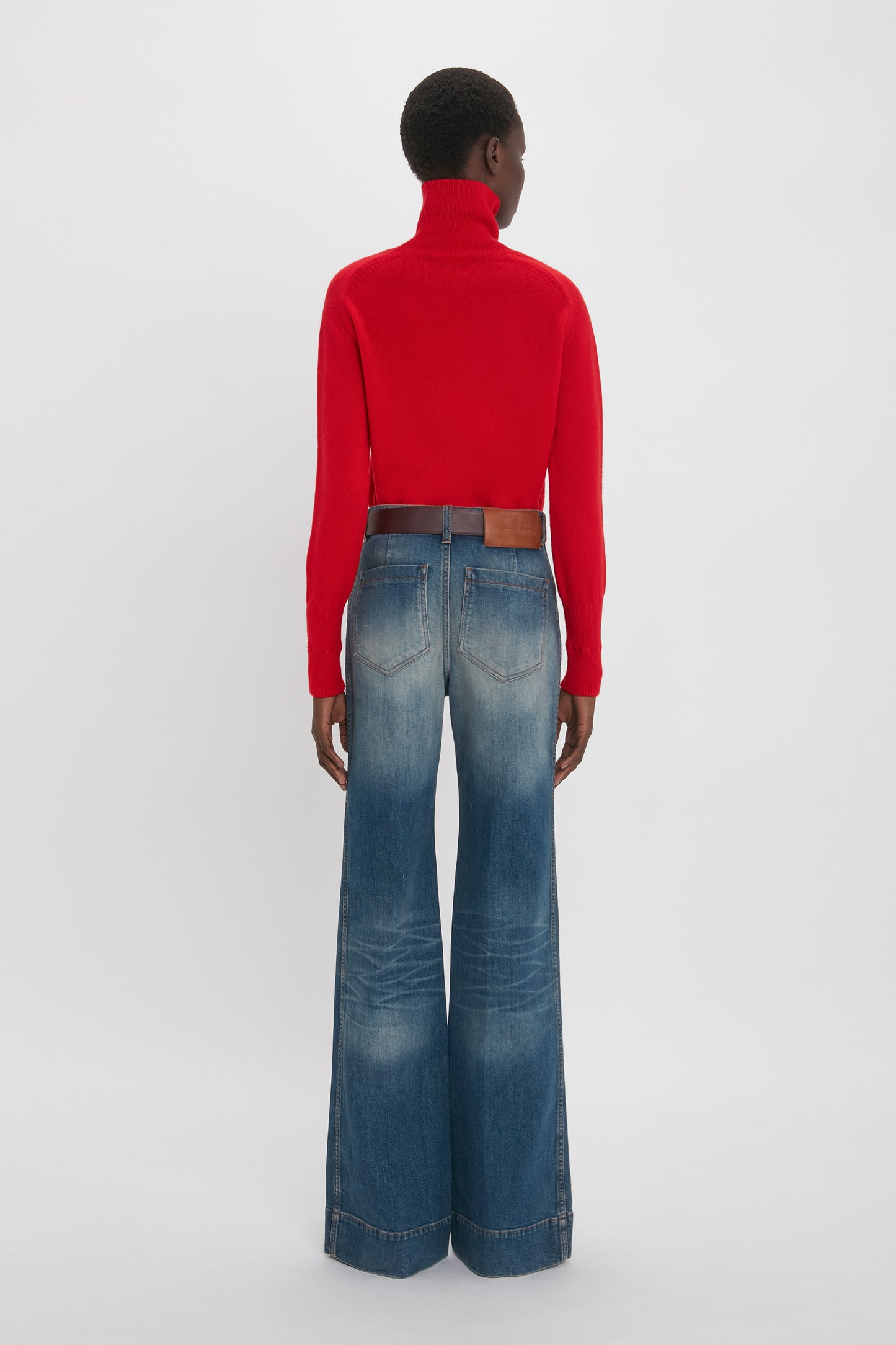 Person facing away, wearing a Victoria Beckham red turtleneck sweater and Alina High Waisted Jean In Heavy Vintage Indigo Wash.
