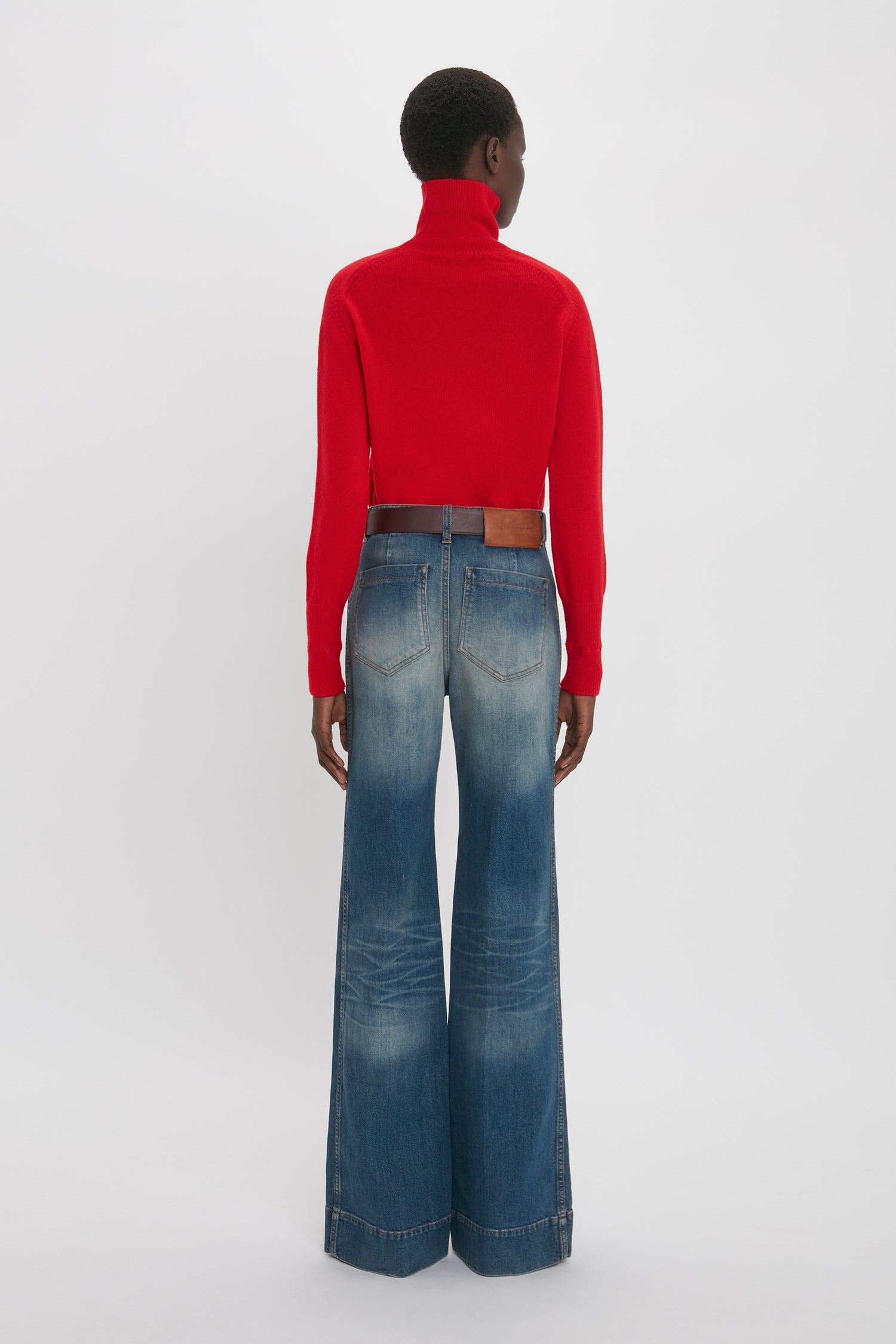Person facing away, wearing a Victoria Beckham red turtleneck sweater and Alina High Waisted Jean In Heavy Vintage Indigo Wash.