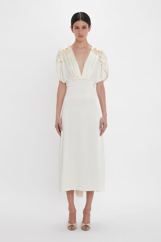 Person wearing a Victoria Beckham Exclusive V-Neck Ruffle Midi Dress In Ivory with puffed short sleeves and open-toe shoes, standing against a plain white background.
