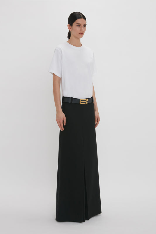 A woman stands against a plain background, wearing an asymmetric relaxed fit t-shirt, black high-waisted palazzo pants, and a slim black belt with a gold buckle.