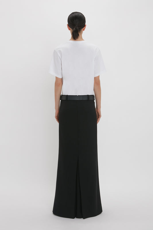 A woman seen from the back wearing a white asymmetric relaxed fit t-shirt and Victoria Beckham black wide-legged pants, standing against a plain white background.