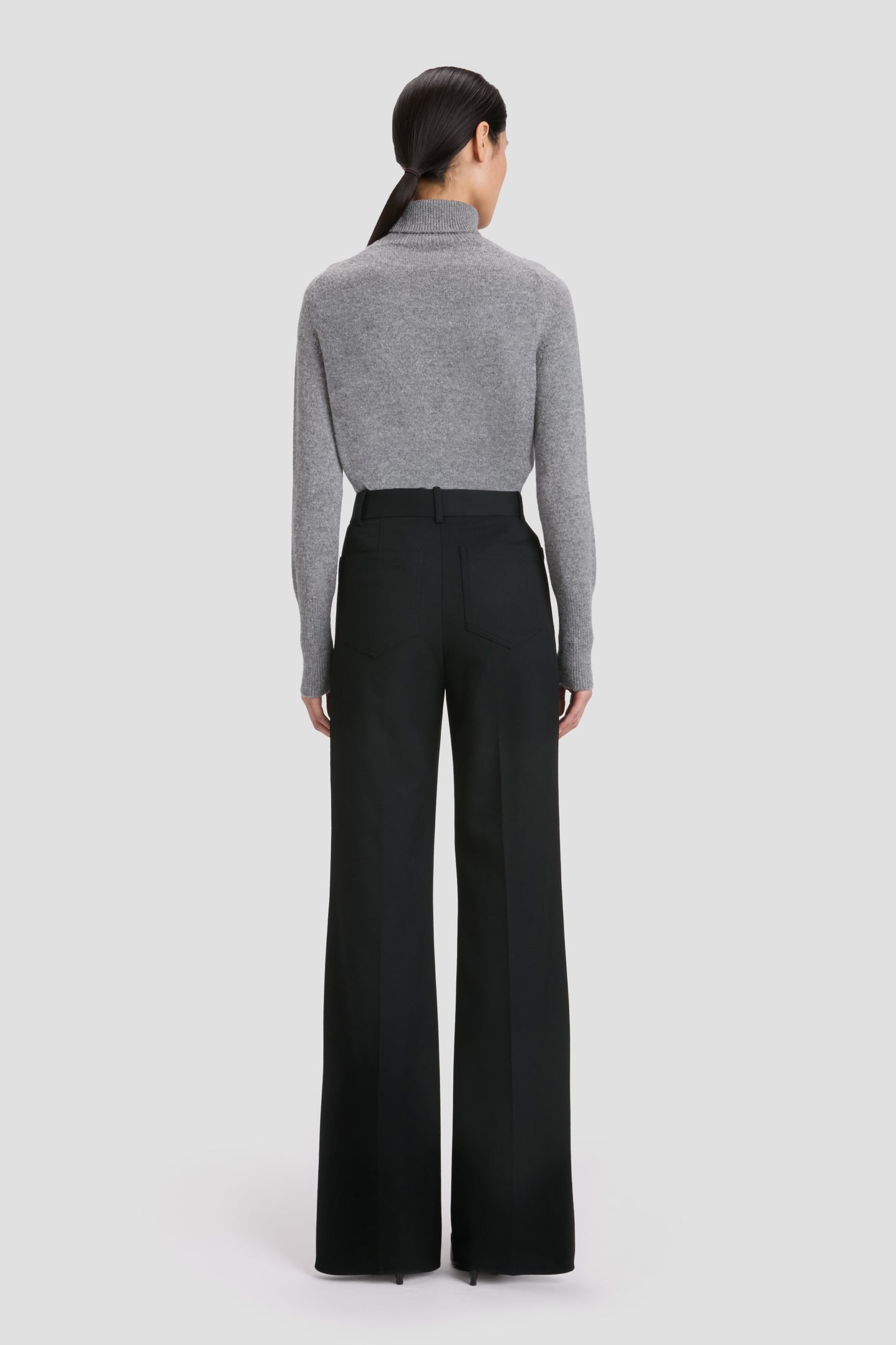 A person stands facing away, wearing Victoria Beckham’s BAO TEST - Jeans Short against a plain background.
