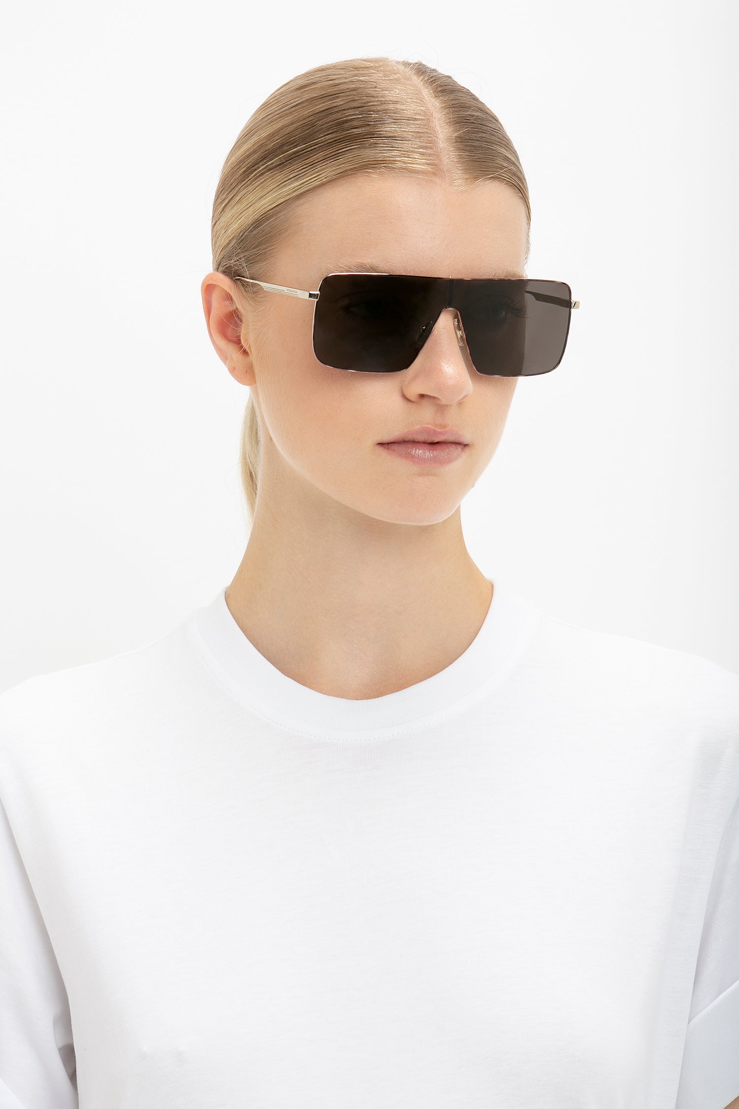 Person with blonde hair wearing a white shirt and large Rectangular Visor In Gold-Smoke by Victoria Beckham, looking forward against a plain white background.