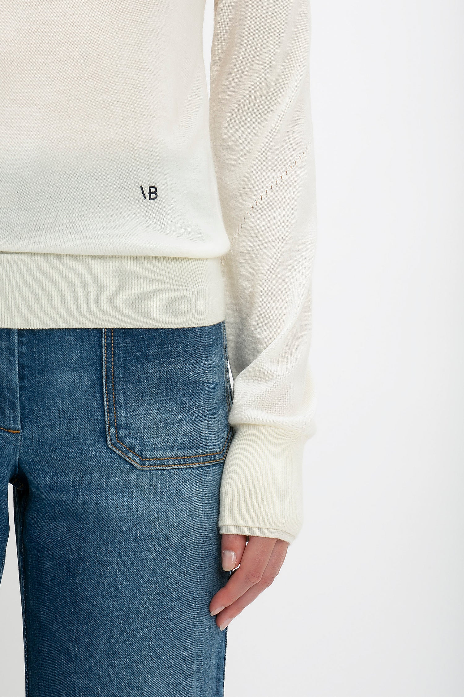 Close-up of a person wearing a Victoria Beckham Merino Crew Jumper in Ivory and blue jeans, focusing on the sweater's cuff and the top of the jeans.