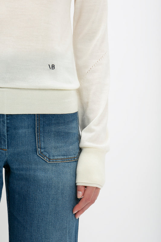 Close-up of a person wearing a Victoria Beckham Merino Crew Jumper in Ivory and blue jeans, focusing on the sweater's cuff and the top of the jeans.