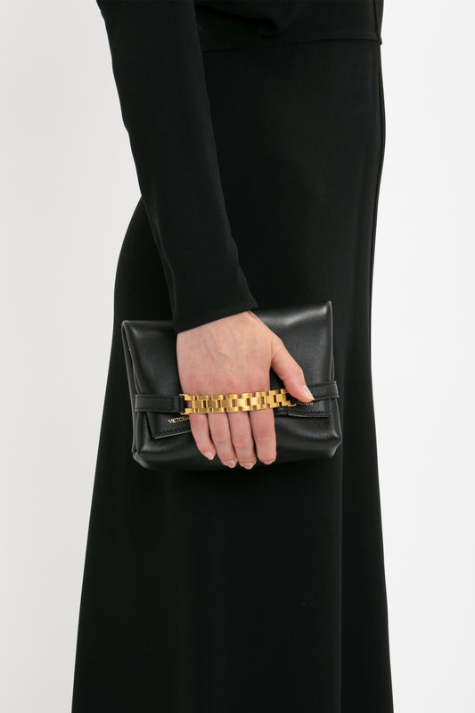 Woman in a black Victoria Beckham Dolman Midi Dress holding a small black clutch with a gold chain.
