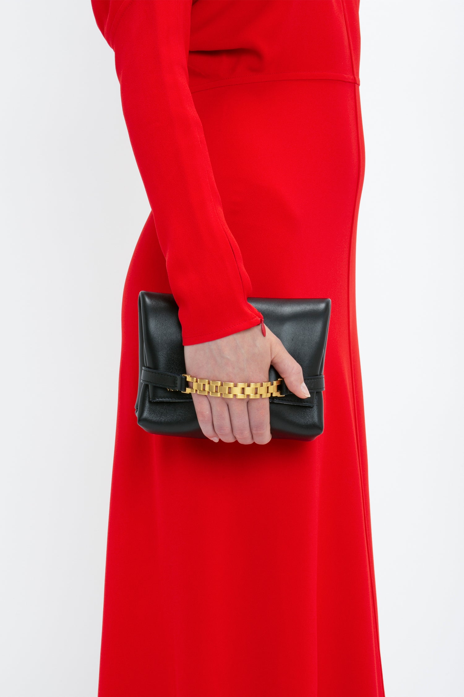 A woman in a red Victoria Beckham Dolman Midi Dress holds a black clutch with a gold chain handle.