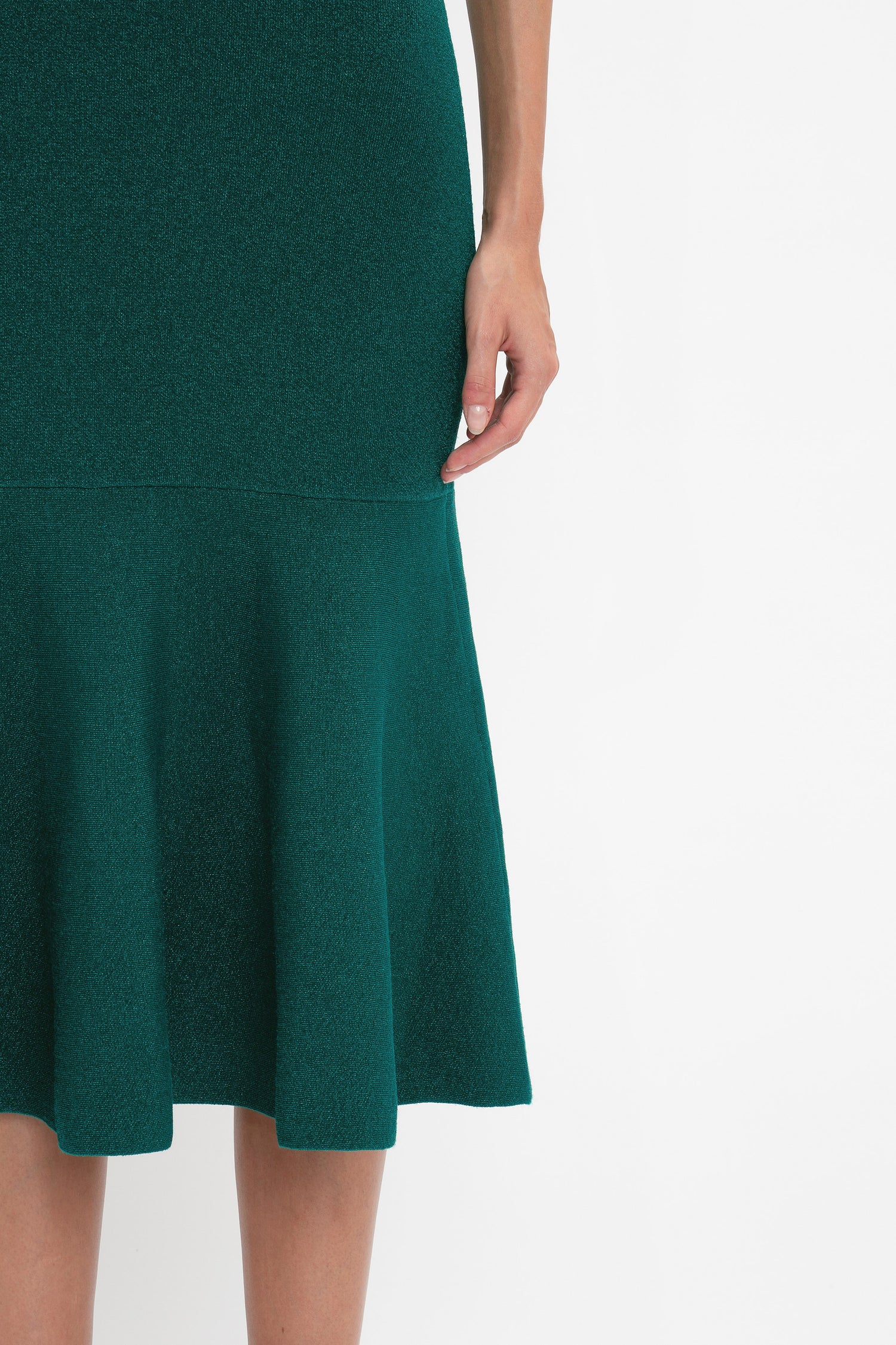 A person wearing a dark green, flattering VB Body Sleeveless Dress In Lurex Green by Victoria Beckham with a form-fitting design, showcasing only the lower torso, hand, and upper thigh. A perfect addition to your new-season wardrobe.