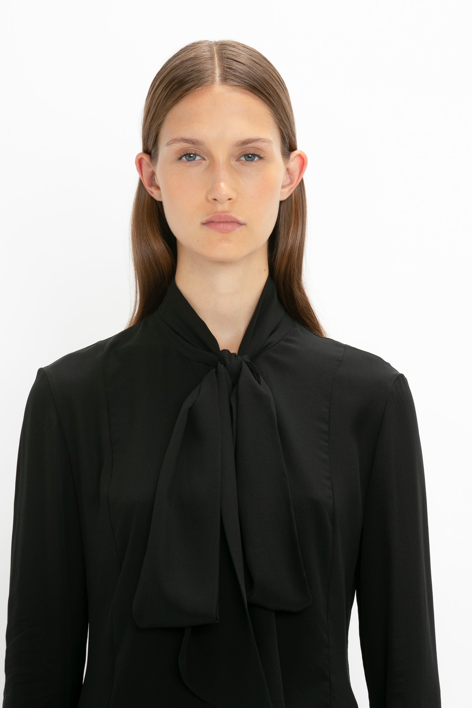 A person with long straight hair wearing a Pleat Cuff Blouse In Black by Victoria Beckham and a knotted necktie stands against a plain white background.