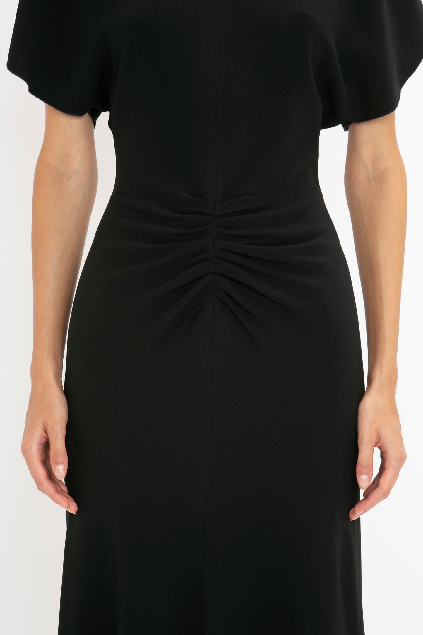 Woman wearing a Victoria Beckham black dress with short flutter sleeves and a gathered waist detail, viewed from a close midsection angle focusing on the dress design.