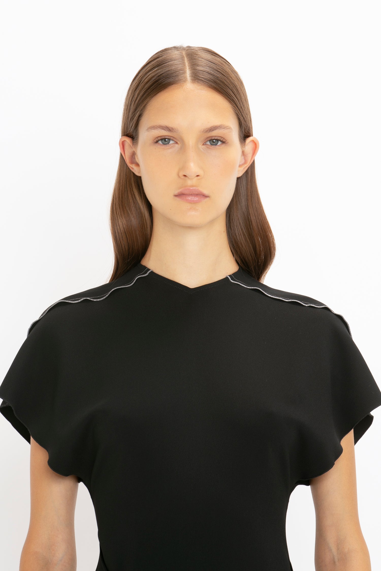Portrait of a woman with straight brown hair and a Short Sleeve Tie Detail Dress In Black by Victoria Beckham, featuring a scalloped neckline and front-tie detail, against a white background.
