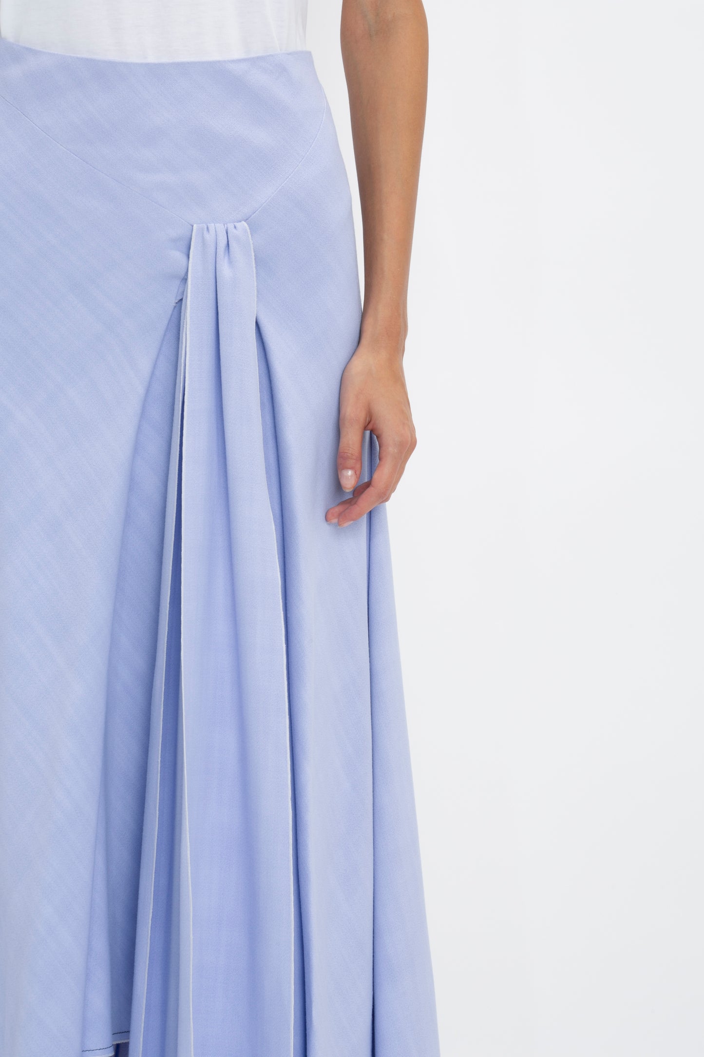 Person wearing a light blue Asymmetric Tie Detail Skirt In Frost by Victoria Beckham with pleated detail, showcasing a portion of their right arm and hand against a plain background, embodying modern femininity.