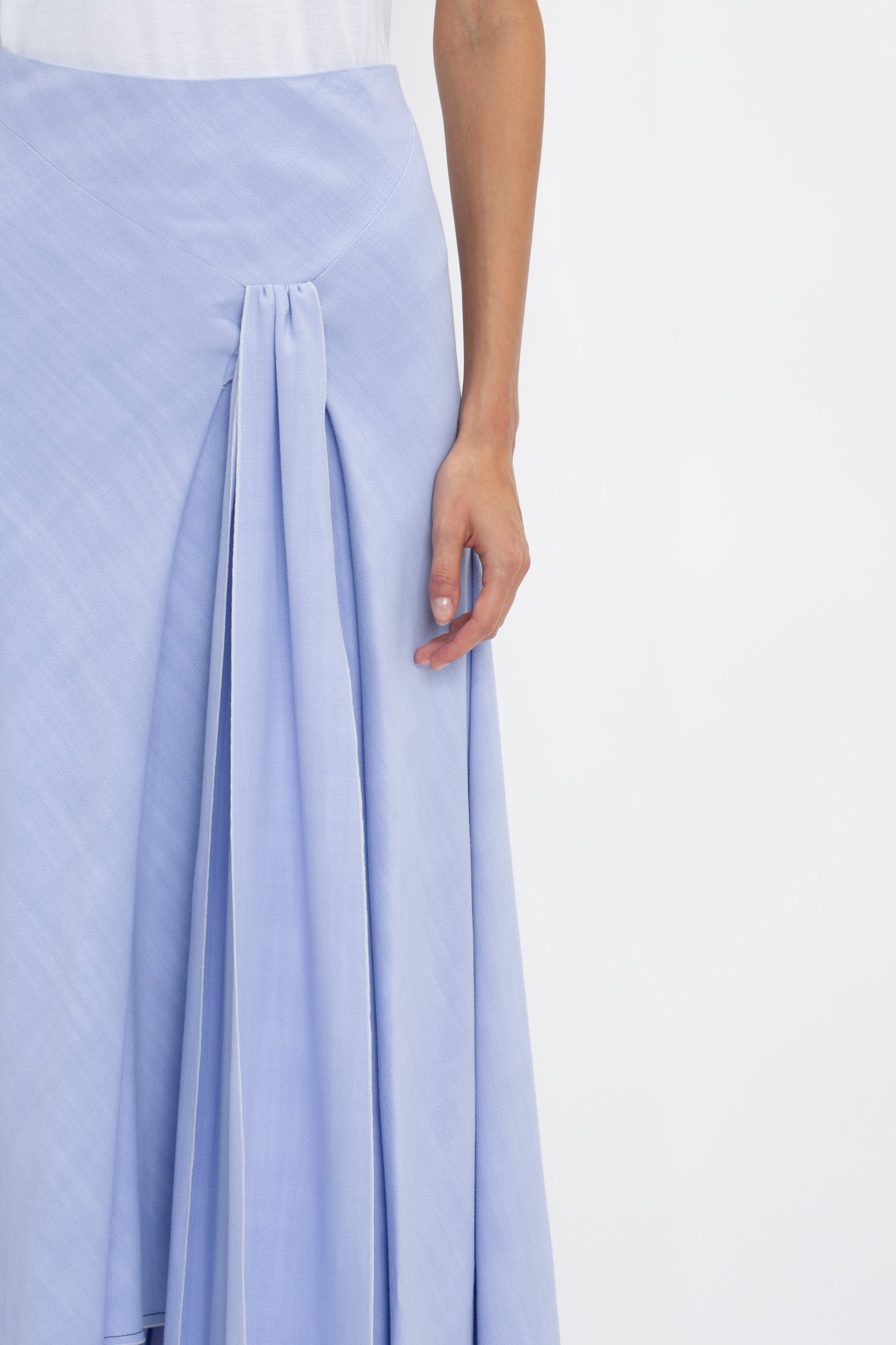 Person wearing a light blue Asymmetric Tie Detail Skirt In Frost by Victoria Beckham with pleated detail, showcasing a portion of their right arm and hand against a plain background, embodying modern femininity.
