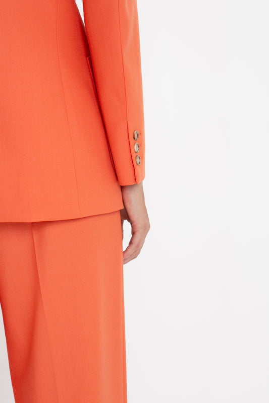 Close-up of a person wearing a Victoria Beckham Patch Pocket Jacket In Papaya with detailed buttons on the sleeve, against a white background.