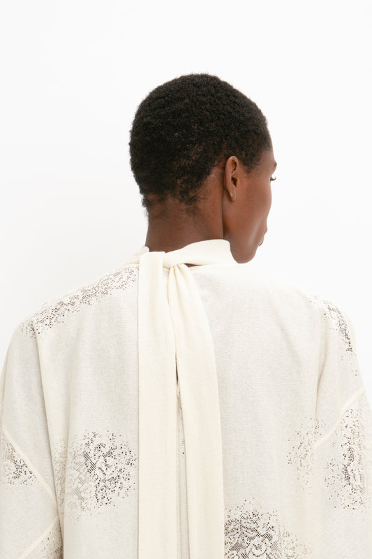 Rear view of an African American man wearing an elegant white jacket with blouson sleeves and lace details, looking to the side against a plain background of a Victoria Beckham Asymmetric Gather Detail Top in Cream.
