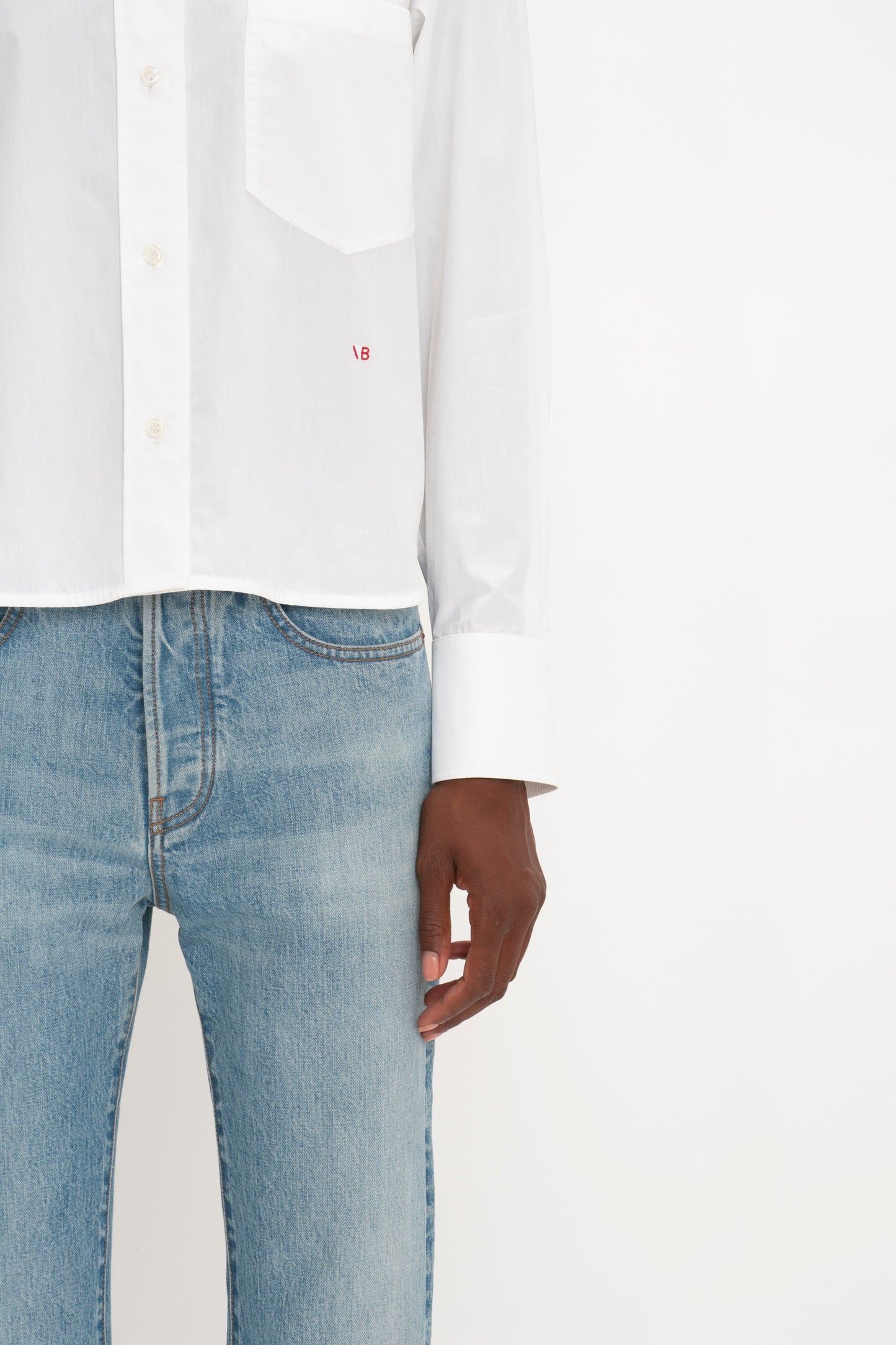 Close-up of a person wearing a Victoria Beckham cropped long sleeve shirt in white and blue jeans, focusing on the torso and left hip area.